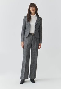 Šedý tailored oblek se strukturovaným sakem, širokými kalhotami a bílým rolákem pod ním. Černé kotníkové boty na podpatku dotvářejí celkový vzhled.