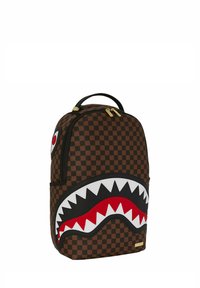 Zaino a quadretti marrone con un grande design della bocca di uno squalo bianco e nero, dettagli rossi, doppie cerniere e una maniglia superiore per il trasporto.