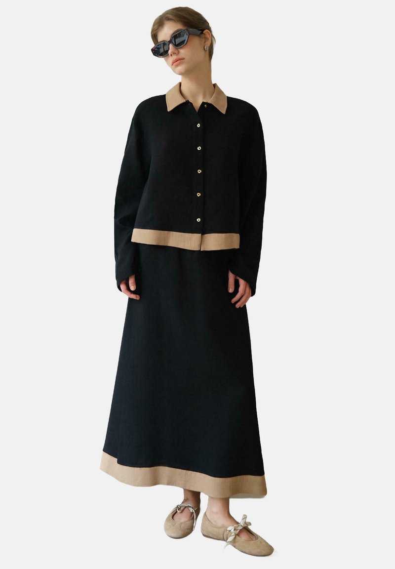 Sort strikket cardigan med cremefarvet krave og kant, parret med en matchende sort nederdel med en cremefarvet kant. Model iført sorte solbriller.