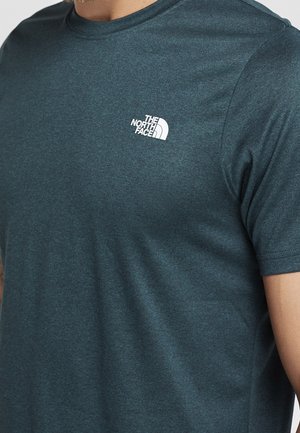 T-shirt teal à manches courtes et col arrondi, fabriqué en tissu texturé et évacuant l'humidité. Présente un logo blanc de "The North Face" sur la poitrine.