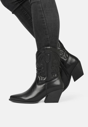 Botas de cowboy de cuero negro con punta afilada, tacón cuadrado y costuras decorativas. Cuentan con un zipper en el costado para facilitar su uso.