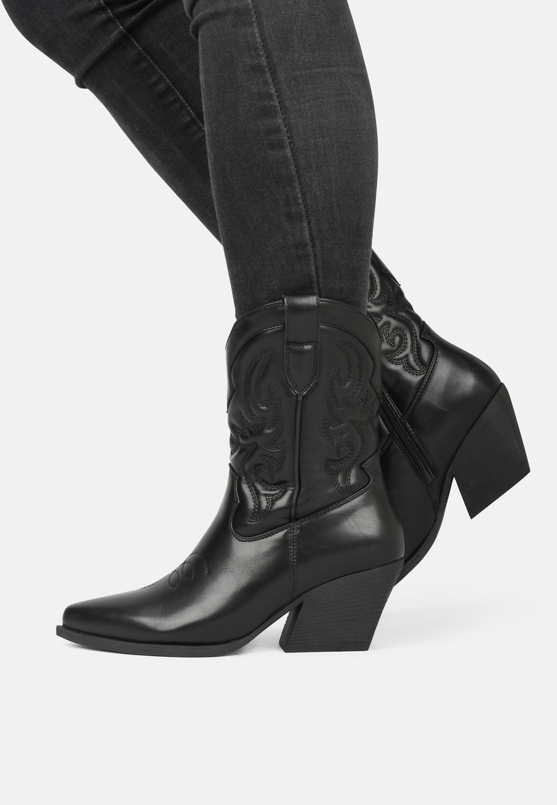 Botas de cowboy de cuero negro con punta afilada, tacón cuadrado y costuras decorativas. Cuentan con un zipper en el costado para facilitar su uso.