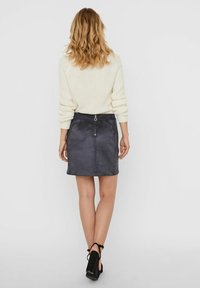 Mini gonna in suede nera con tasche laterali e zipper sul retro, abbinata a un maglione lavorato a maglia crema e tacchi neri spessi.