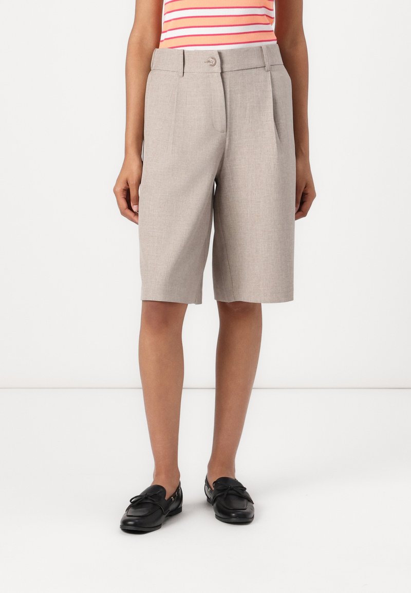 Lys grå skreddersydde shorts med folder, knappelukking og sidelommer, sammen med svarte loafers. Jevn tekstur.