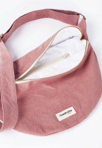 Sac en toile rose avec une forme courbée, fermeture éclair dorée et intérieur blanc. Équipé d'une petite étiquette et d'une bandoulière ajustable.