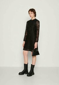 Black lace dress with long sleeves, straight cut, and scalloped neckline. Paired with black ankle boots and a small black handbag.