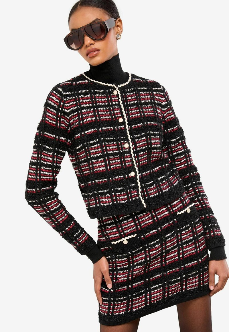 Černý a červený kostkovaný tvídový kabát s krátkým střihem, perlovými knoflíky a laděnou sukní. Má žebrované manžety a texturovaný vzor.