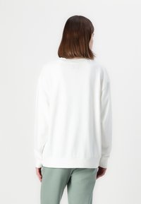 Sweatshirt en coton blanc avec une coupe décontractée, des manches longues et un ourlet côtelé. Présente un design simple, sans marque ni motifs visibles.