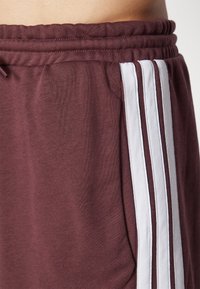 Burgundy sweatpants gjorda av mjuk bomull, med vita vertikala ränder på sidorna och ett elastiskt midjeband med snörning.