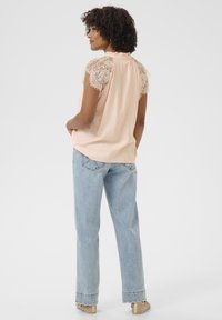 Blusa pesca con maniche corte in pizzo, scollatura rotonda e dettagli arricciati sul retro, abbinata a jeans a gamba larga blu chiaro.