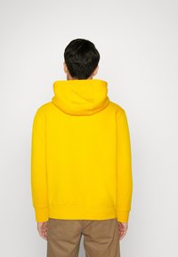 Sudadera amarilla con capucha y un corte relajado, que cuenta con un bajo y puños acanalados, fabricada en un tejido suave, con una capucha grande y redondeada.