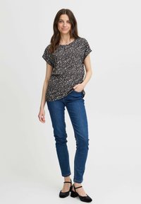 Haut noir avec motif abstrait blanc, manches courtes, coupe décontractée. Associé à un jean skinny bleu et des escarpins à brides noires. Design simple.
