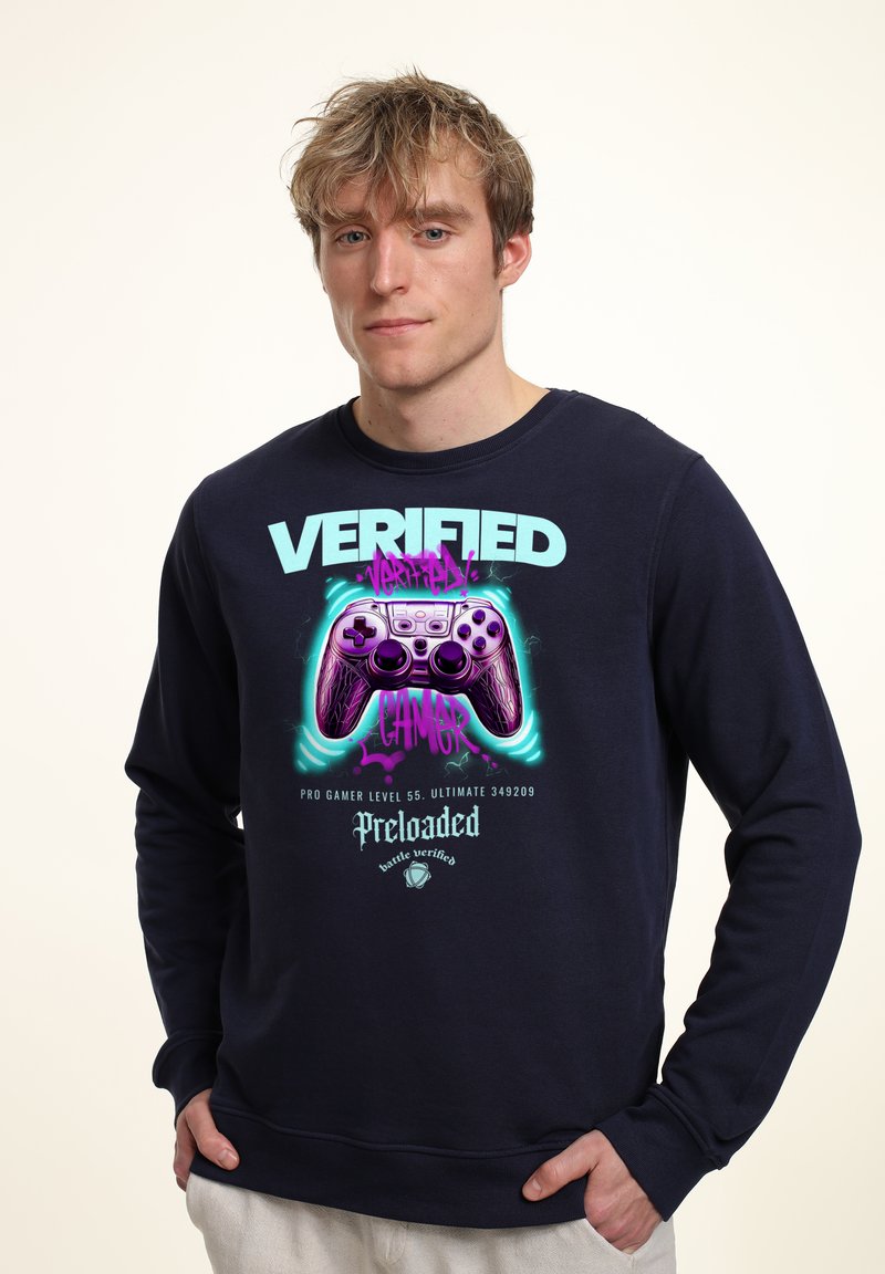 Felpa navy con grafica di un controller di gioco viola e testo "VERIFIED GAMER" in turchese e rosa. Tessuto morbido, design con colletto a girocollo.