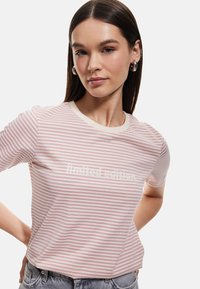 Camiseta a rayas en rosa claro y blanco, con un cuello redondo neutro y el texto "edición limitada" en el centro. Material de algodón suave.
