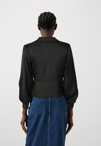Blusa nera in chiffon con maniche a sbuffo e colletto, abbinata a una gonna di jeans con due tasche posteriori e taglio dritto.