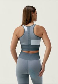 Šedá sportovní podprsenka a legíny v setu s texturovaným vzorem, designem na závodní záda a barevnými bloky v různých odstínech šedé.