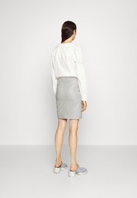 Blusa blanca con mangas abullonadas, minifalda de cuero gris y mules grises con suelas blancas gruesas. El fondo es blanco liso.