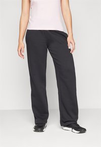Black sweatpants with a loose fit, side pockets, and elastic waist. Paired with a light pink fitted top and black athletic shoes.