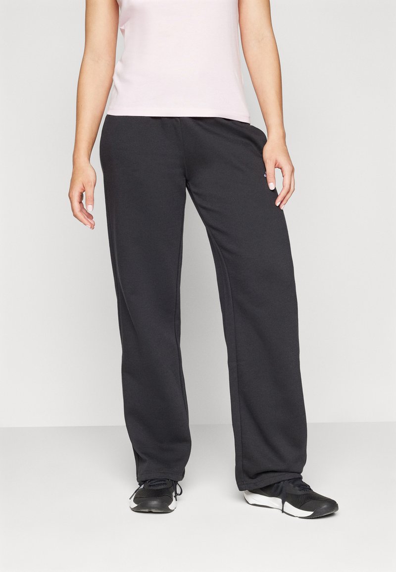 Black sweatpants with a loose fit, side pockets, and elastic waist. Paired with a light pink fitted top and black athletic shoes.