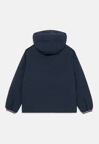 Chaqueta impermeable azul marino con capucha, puños elásticos y un diseño sencillo. Presenta una textura suave y sin logotipos ni adornos visibles.