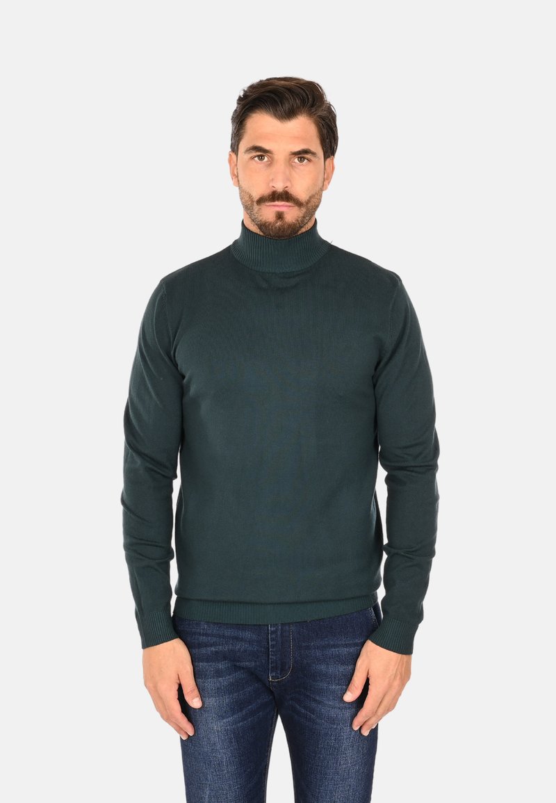 Maglione a collo alto verde scuro in maglia a coste. Linea aderente con maniche lunghe e collo alto. Abbinato a jeans blu.