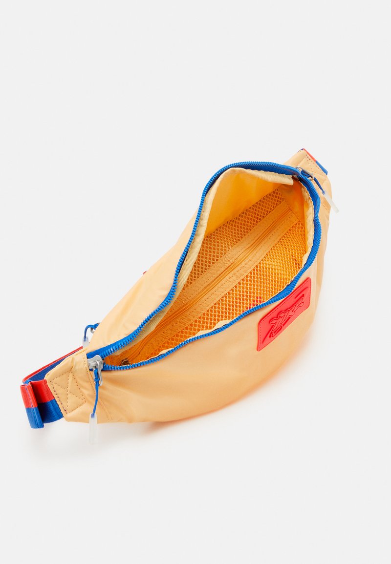 Sac banane en nylon orange vif avec une fermeture éclair bleue. À l'intérieur, il dispose d'une poche en maille et d'un petit compartiment zippé pour l'organisation.