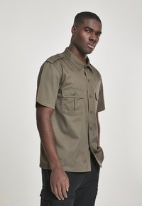 Camisa de manga corta de color verde oliva, hecha de mezcla de algodón, con dos bolsillos frontales, cierre de botones y un cuello clásico. Textura suave.