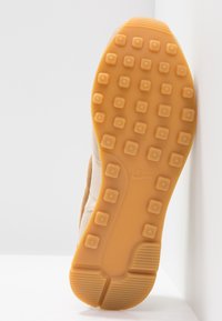 Semelle en caoutchouc orange d'une basket avec des crampons carrés et un logo Nike, présentée sur fond blanc.