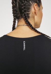 Svart atletisk topp i andningsbart tyg, med rund halsringning och meshstruktur. "ICANWILL"-logotyp på baksidan.