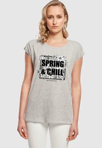 Grå kortærmet t-shirt med et sort blomsterdesign og teksten "SPRING & CHILL" samt "ONLY GOOD VIBES" i fed skrift.