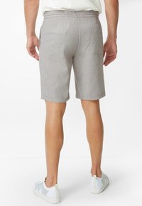 Grau gestreifte Shorts mit lockerem Schnitt, ausgestattet mit einer Gesäßtasche und einer glatten Textur, kombiniert mit weißen Sneakern.