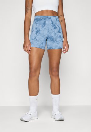 Höga blåa tie-dye atletiska shorts med en mjuk textur och en figurnära design, kombinerat med vita strumpor och skor.