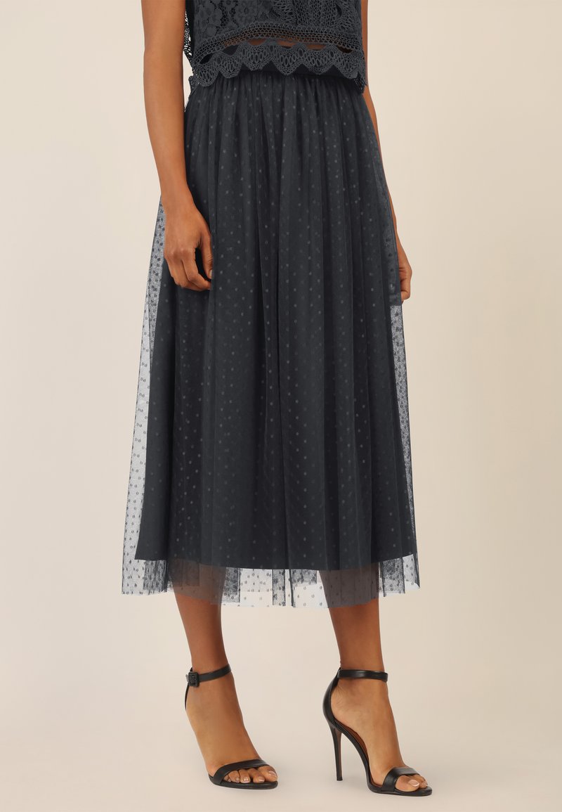 Gonna midi in tulle navy con motivo a pois, cintura elastica, design a strati, texture trasparente e sottogonna solida. Abbinata a tacchi neri.