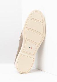 Suola di scarpa in suede marrone chiaro con una suola in gomma bianca, caratterizzata da un motivo testurizzato e dettagli di branding al centro.