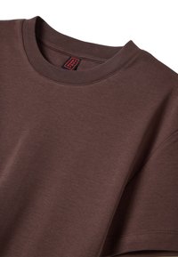 T-shirt in cotone marrone con scollatura a girocollo rigata e cuciture sulle spalle. Presenta una piccola etichetta rossa vicino al colletto. Tessuto liscio.
