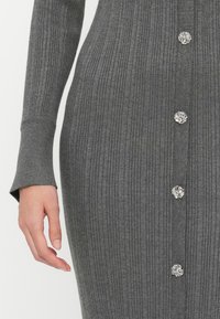Γκρίζα ριγωτή πλεκτή φόρμα με μακριά μανίκια, που διαθέτει διακοσμητικά μεταλλικά κουμπιά κατά μήκος του μπροστινού μέρους και υφή υφάσματος.