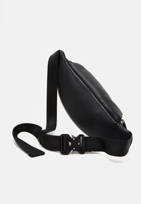 Sac bandoulière en cuir noir avec une forme arrondie, présentant une surface texturée, une sangle ajustable et une fermeture à boucle en plastique.