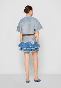 Top de cuero azul claro recortado con mangas cortas, combinado con una falda de mezclilla de capas con dobladillo deshilachado y parche de estrella. Mules azules.