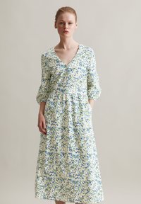 Blumenkleid in Midi-Länge aus leichtem Stoff, mit V-Ausschnitt, Dreiviertelärmeln und blauen sowie grünen Blumenmustern auf einem cremefarbenen Hintergrund.