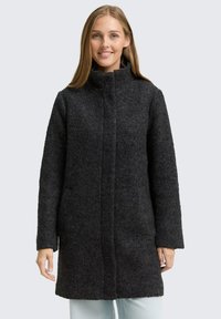 Manteau en laine noire avec un col haut, surface textur�ée, manches longues et coupe droite. Présenté sur un fond gris clair.