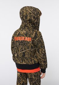 Giacca con cappuccio in un motivo mimetico scuro con il testo arancione "TIMBERLAND" sul retro; polsini e orlo a costine; morbido texture del tessuto.