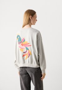 Grijze sweatshirt met lange mouwen, voorzien van een kleurrijke papegaai-afbeelding op de achterkant. Gemaakt van zachte stof, relaxed fit, ribgebreide manchetten en zoom.