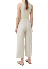 Lichtbeige tanktop met ribbelstructuur; wijde beige broek met achterzakken; model draagt platte gevlochten sandalen.