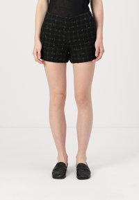 Juodi tweed šortai su tekstūruotu raštu, turi prigludusią juosmenį ir šiek tiek skeltą kraštą. Derinama su juodais loafers.
