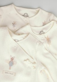 Drei cremige Babystrickjacken aus weichem Stoff, mit hellrosa Tupfen, gestickten Tiermotiven und dekorativen Knöpfen.