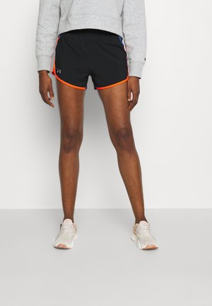 Person wearing black athletic shorts with orange trim, gray sweatshirt, and white running shoes standing against a plain white background.