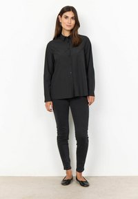 Černá košile na knoflíky s dlouhými rukávy, s klasickým límečkem a hladkou texturou, doplněná černými skinny džíny a černými balerínami.