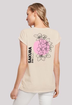 Beige t-shirt featuring a floral design with pink accents and text "SAKURA" on the back. Short sleeves and a soft texture.