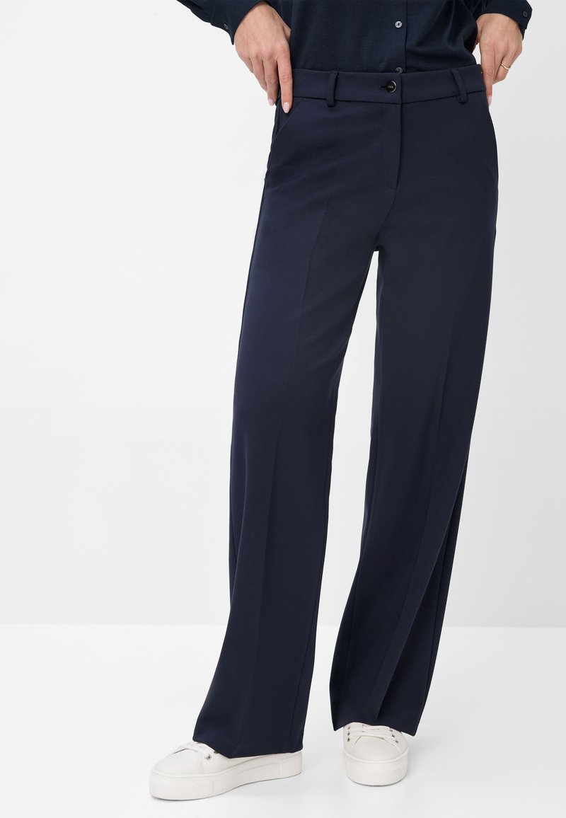 Navy blue wide-leg trousers with a straight cut, featuring a smooth texture, a waistband, and a single button closure. White sneakers visible.