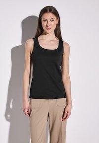 Schwarzes Tanktop mit rundem Halsausschnitt, aus einem glatten, dehnbaren Stoff gefertigt. Kombiniert mit beigen, weit geschnittenen Hosen, die ein minimalistisches Design zeigen.